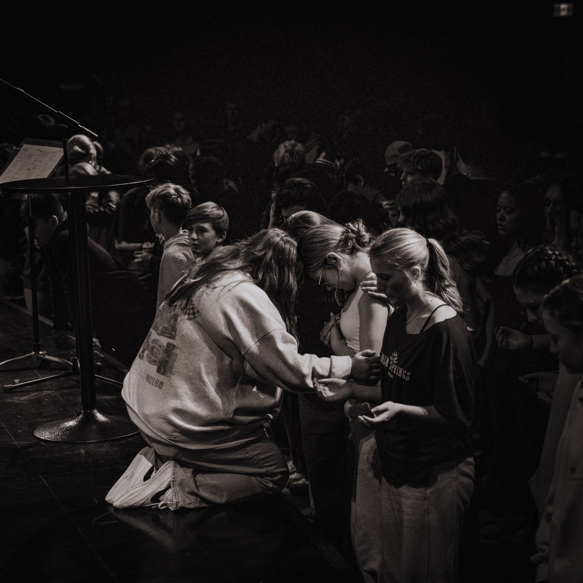 Kneeling in prayer with students at the front of the stage